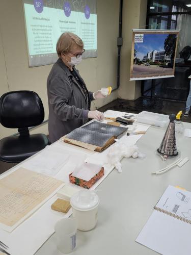Colaboradora Ana Paula do SPD- Seção de Preservação de Documentos explicando como se da o processo de limpeza e higienização dos documentos.