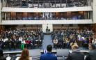 Em primeiro plano, mesa de abertura de costas para a foto. Em segundo plano, a plateia presta atenção.
