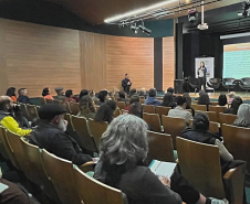 Público sentado em auditório assiste palestrante Marina Braga, que está em cima de um palco.