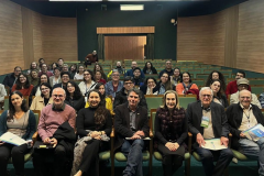 Público e palestrantes sorrindo e olhando para a câmera.