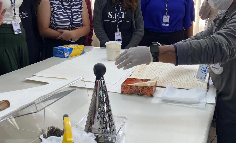 A colaboradora Sabrina Maria da Silva, da Seção de Preservação de Documentos (SPD), apresenta os trabalhos desenvolvidos em seu setor, detalhando as técnicas de conservação e restauração aplicadas para garantir a integridade e a longevidade dos documentos históricos.