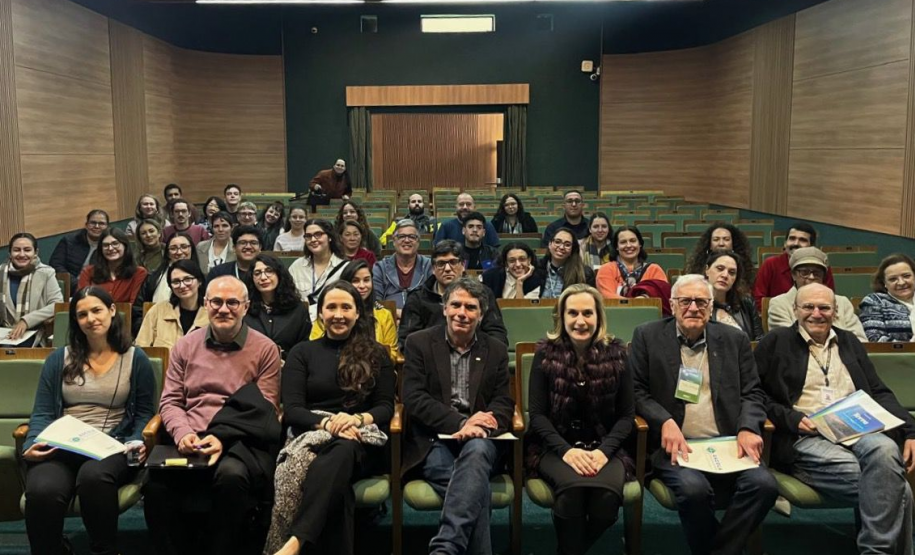 Público e palestrantes sorrindo e olhando para a câmera.
